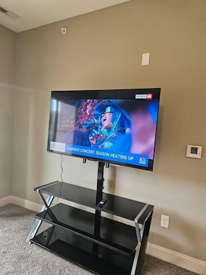 A flat-screen TV mounted on a wall with a stand below it. - 1-bed by Jordan Creek & Top Golf (West Des Moines)