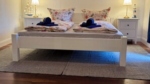 Un lit avec une literie à motifs floraux, deux tables de chevet avec des lampes et un plancher en bois.