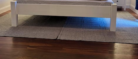 Uma cama com roupa de cama floral, duas mesas de cabeceira com abajures e piso de madeira.