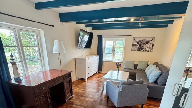 Un vaste espace de vie doté d’un plancher en bois, d’un ensemble de canapés, d’un téléviseur et d’un bureau avec une lampe.