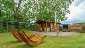 Une cabane en bois dotée d’un patio, entourée d’une végétation luxuriante et agrémentée d’une chaise suspendue.