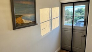 Un couloir avec un plancher en bois, une porte dotée d’une fenêtre et un tableau encadré accroché au mur.