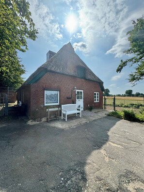 A brick building with a thatched roof, a bench, and a signboard.