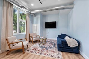 Una sala de estar moderna con un sofá azul, dos sillones, una mesita de centro y un ventanal con cortinas.