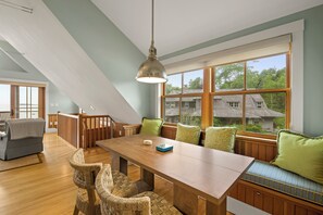 Une pièce spacieuse avec une table à manger en bois, des sièges confortables et de grandes fenêtres donnant sur l’extérieur.