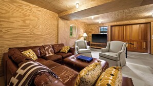 Ein Holzinnenraum mit einem Ecksofa, zwei Sessel, einem Fernseher und einer Holztür.