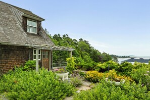 A house with a wooden exterior, a covered porch, and a garden with various plants and flowers. - NEW! Quaint 2BR apt in Harpswell with private beach area and beautiful gardens (Harpswell)