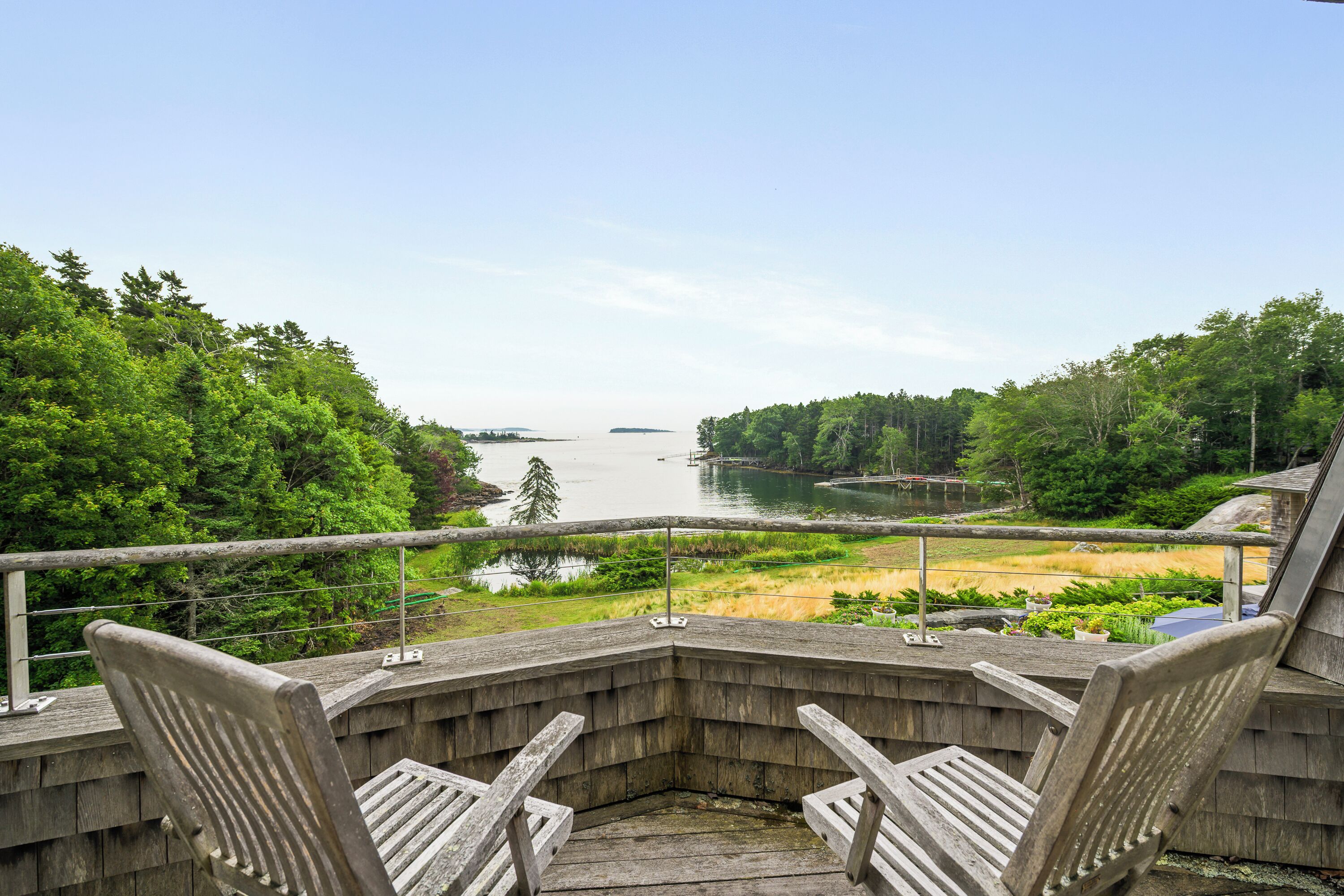 A wooden deck with two chairs facing a lake, surrounded by trees and a distant island.