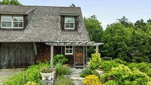 Ein Haus mit überdachter Veranda, Holzgarage und einem Garten mit verschiedenen Pflanzen und Blumen.