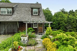 A house with a covered porch, a wooden garage, and a garden with various plants and flowers. - NEW! Quaint 2BR apt in Harpswell with private beach area and beautiful gardens (Harpswell)