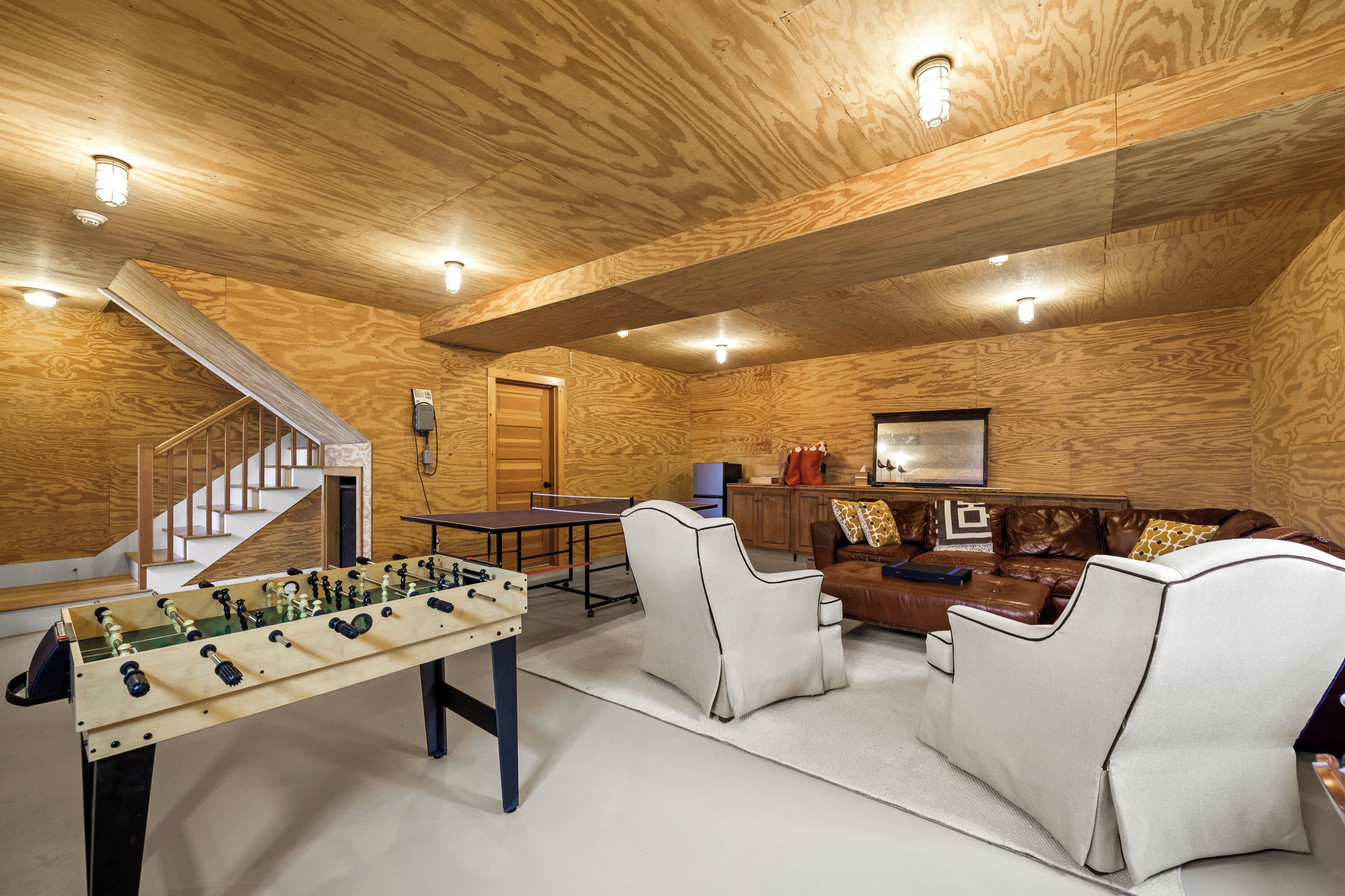 A room with a foosball table, a sofa, a coffee table, and a staircase.