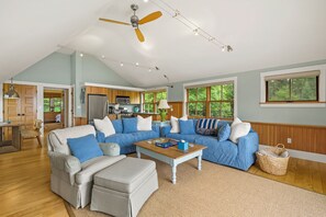 A spacious living room with a large sectional sofa, a wooden coffee table, and a ceiling fan. - NEW! Quaint 2BR apt in Harpswell with private beach area and beautiful gardens (Harpswell)