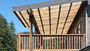 Un terrazza in legno con ringhiera che si affaccia su uno specchio d'acqua, circondata da alberi.