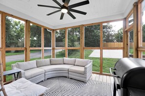 Un espace extérieur aménagé, abrité, avec un canapé incurvé, un barbecue et de grandes fenêtres.