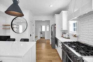 Une cuisine moderne avec des meubles blancs, un îlot central, une cuisinière à gaz et un grand miroir.