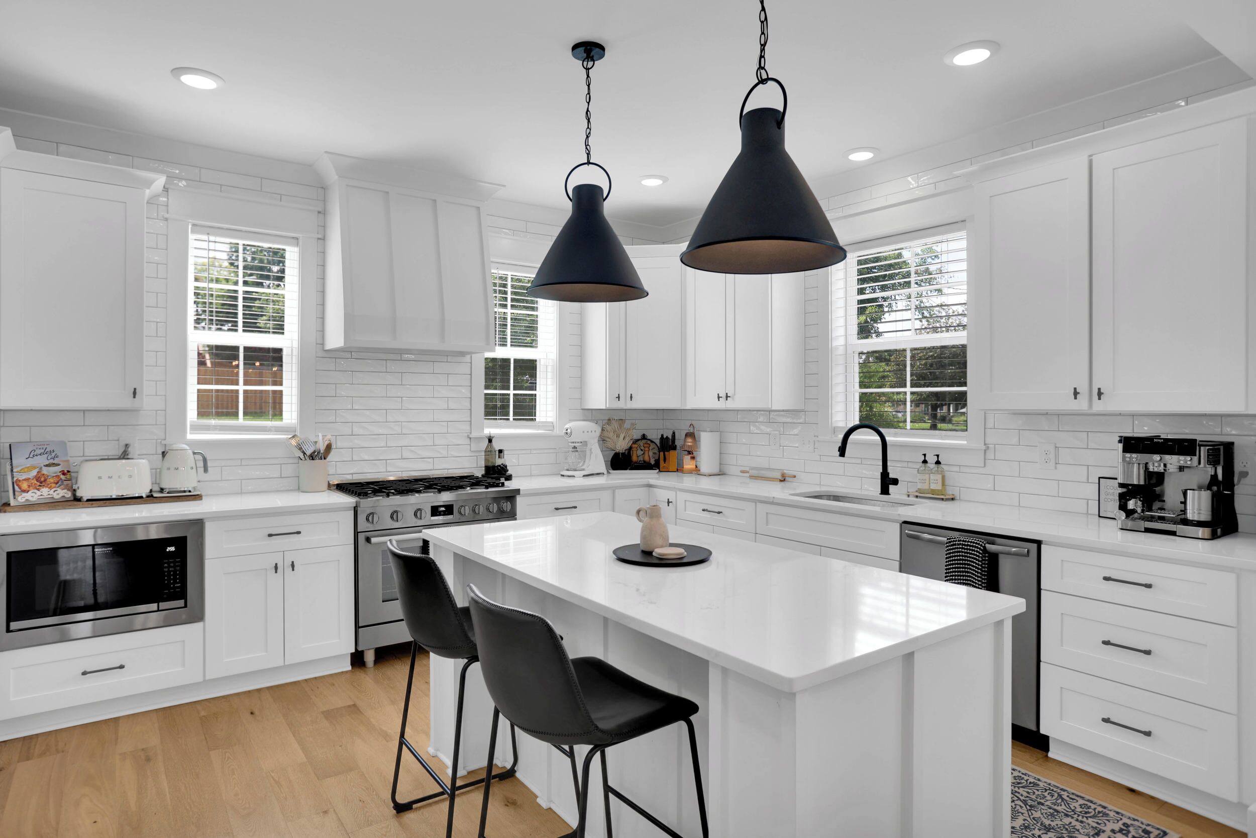 A modern kitchen with white cabinetry, a central island, black pendant lighting, and a coffee machine.
