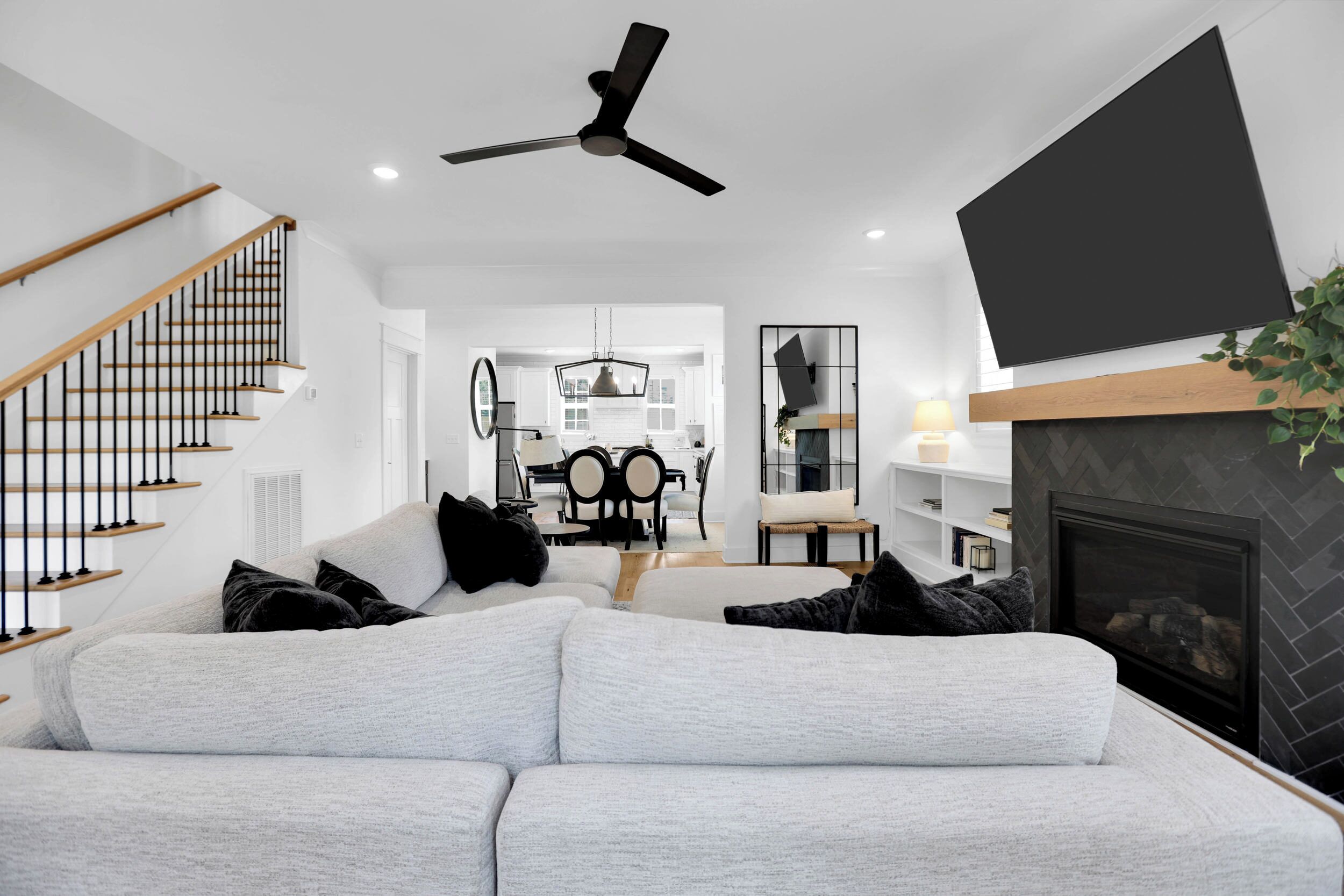 Una sala de estar moderna con un sofá gris, cojines blanco y negro, un ventilador de techo negro y una chimenea.