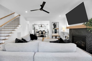 A modern living room with a grey sofa, black and white cushions, a black ceiling fan, and a fireplace. - East Nash Luxe Minutes to Nissan Stadium & Five Points (Nashville)