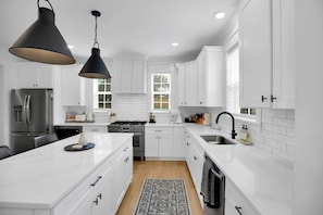 A modern kitchen with white cabinetry, a stainless steel refrigerator, a gas stove, and a black pendant light. - East Nash Luxe Minutes to Nissan Stadium & Five Points (Nashville)