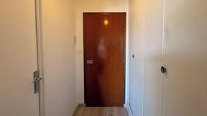 A narrow hallway with a wooden door at the end, white walls, and a light fixture above. - La Madeleine - Balcon - Quartier Château (Bagnoles de l'Orne Normandie)