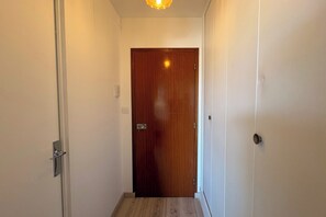A narrow hallway with a wooden door at the end, white walls, and a light fixture above. - La Madeleine - Balcon - Quartier Château (Bagnoles de l'Orne Normandie)