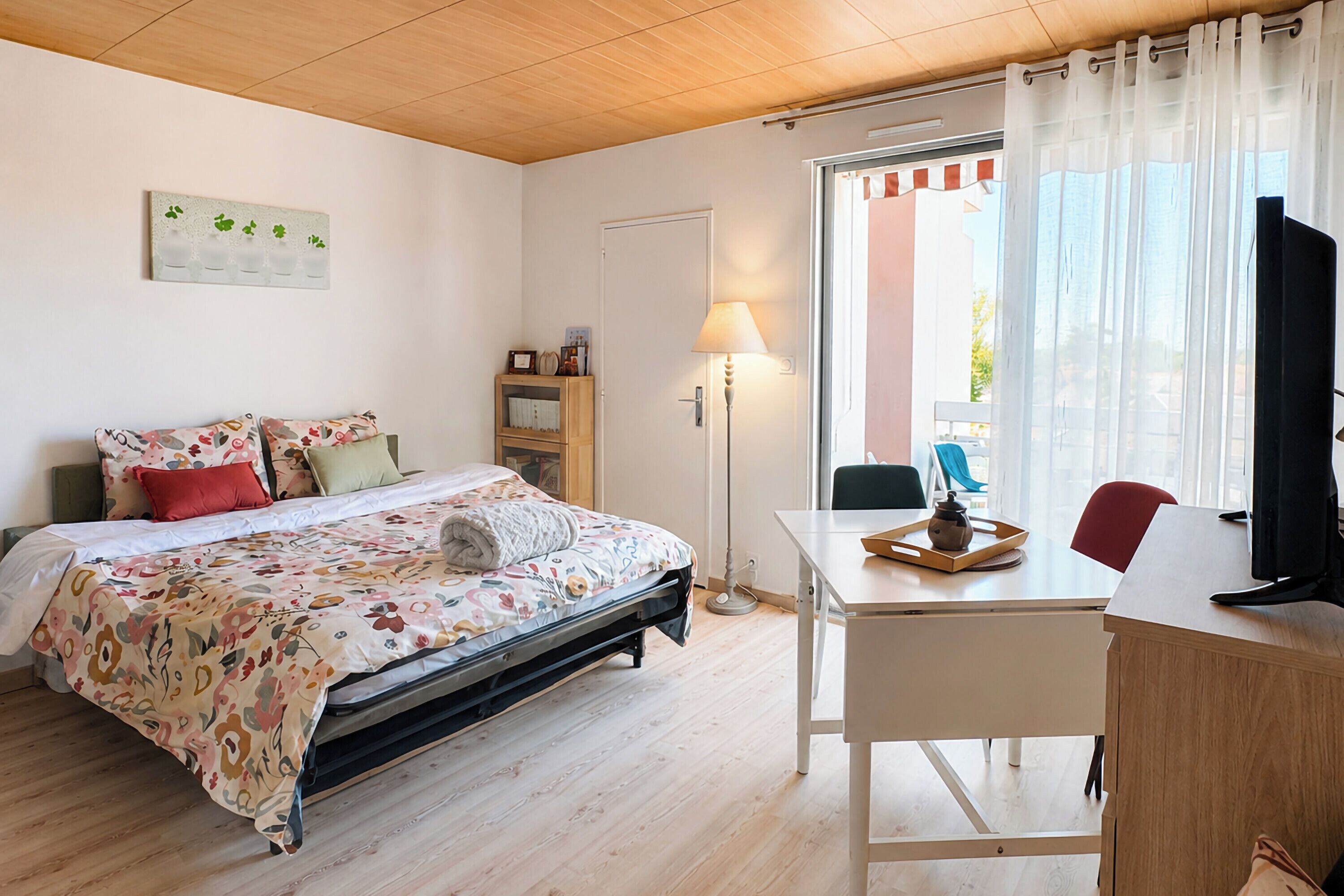 Een slaapkamer met een bed, een bureau, een stoel, een lamp en een raam met gordijnen.