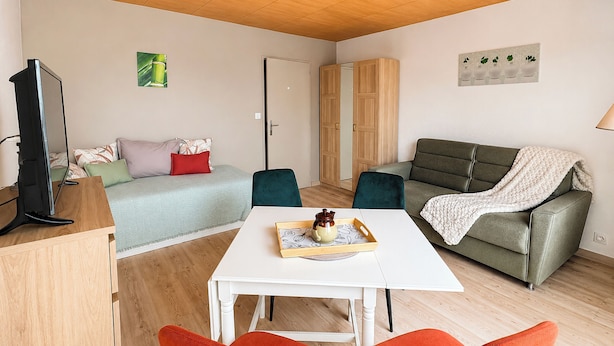 A furnished living space with a sofa, a dining table, a TV, and a wardrobe. - La Madeleine - Balcon - Quartier Château (Bagnoles de l'Orne Normandie)