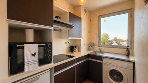 A compact kitchen with a microwave, stove, and washing machine, featuring a window with a view. - La Madeleine - Balcon - Quartier Château (Bagnoles de l'Orne Normandie)