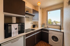 A compact kitchen with a microwave, stove, and washing machine, featuring a window with a view. - La Madeleine - Balcon - Quartier Château (Bagnoles de l'Orne Normandie)