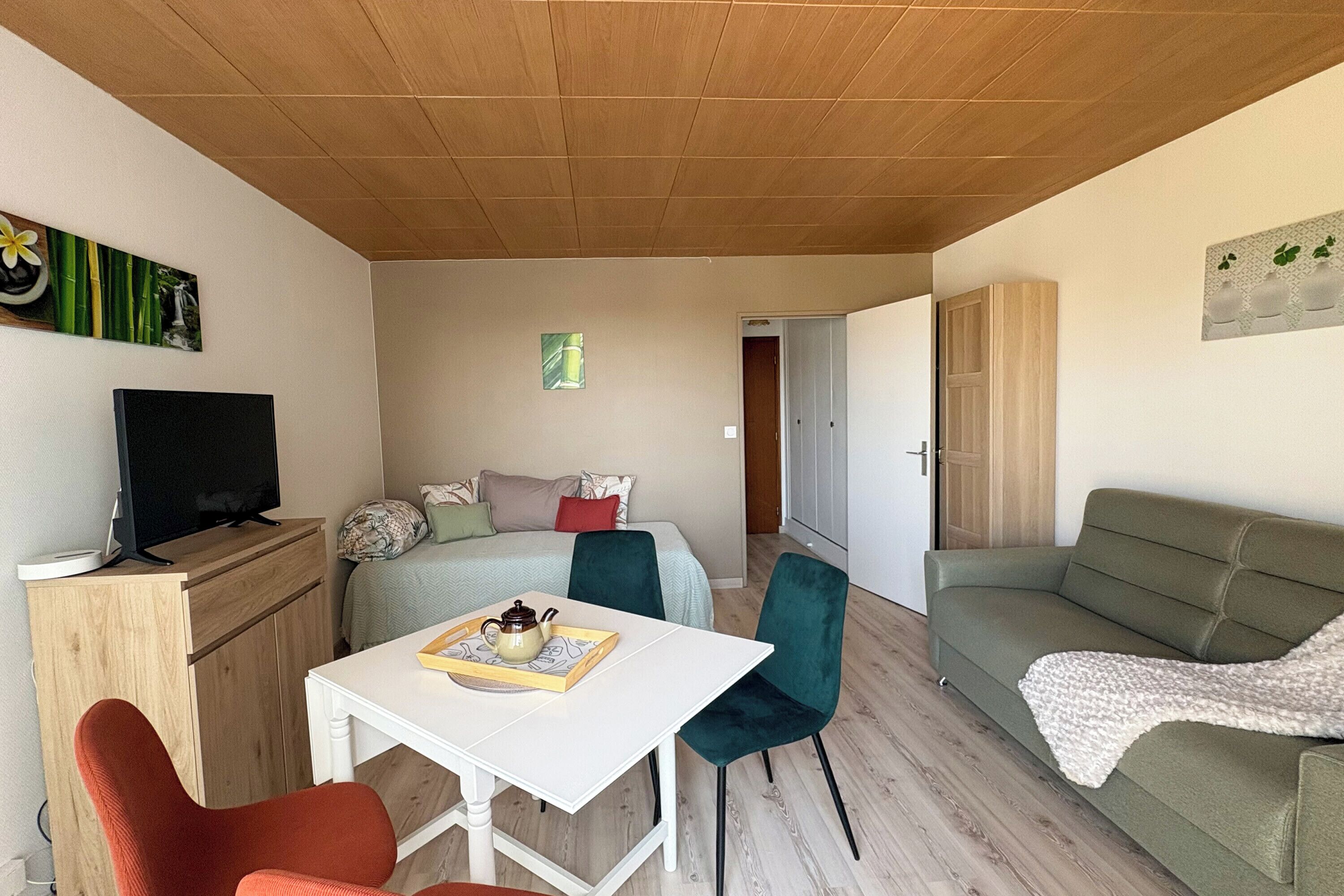 Een kleine kamer met een bed, een bureau, een televisie en een bank.