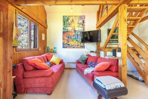 A cozy living room with two red sofas, a television, and a wooden staircase. - Le Lauzat - Petfriendly - Balcon (Villard-Reymond)