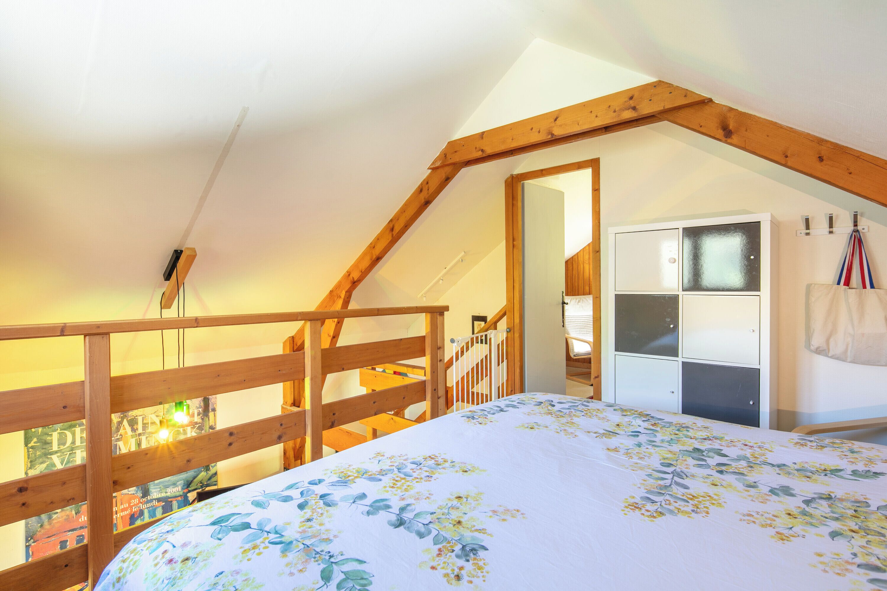 Un dormitorio con techo inclinado, cabecera de cama de madera, armario blanco y vista a través de una puerta abierta.