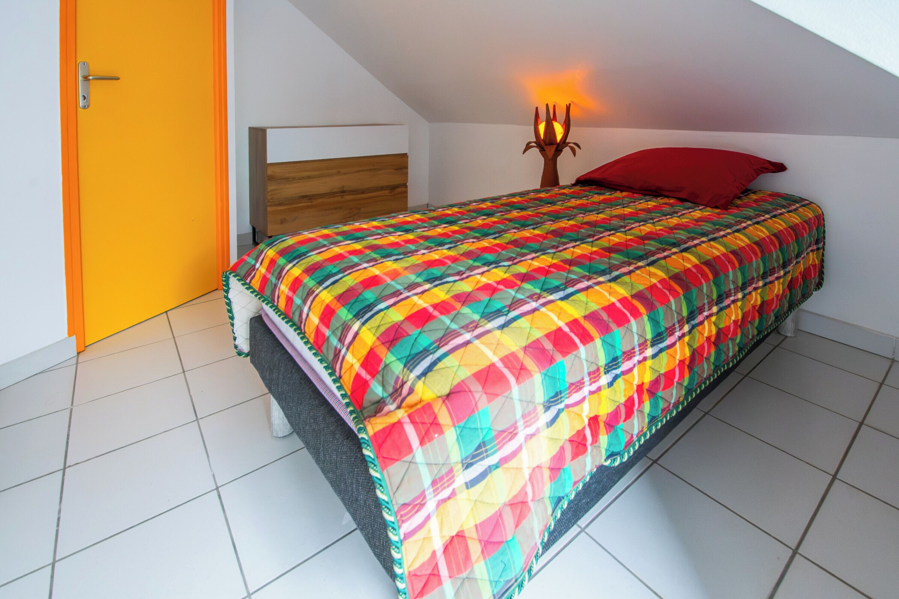 Ein Schlafzimmer mit einem Bett, einem hölzernen Kopfteil, einem roten Kissen und einer Wandlampe.
