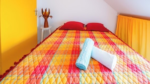 A bed with a colorful quilt, red pillows, and a rolled towel. - Melody - Climatisation - Proche plage (SAINTE ANNE)