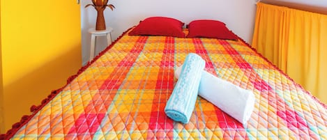 A bed with a colorful quilt, red pillows, and a rolled towel.