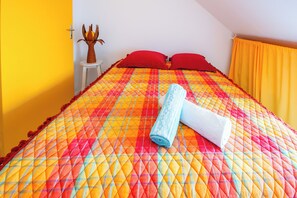 Ein Bett mit einer farbenfrohen Steude, roten Kissen und einem zusammengerollten Handtuch.