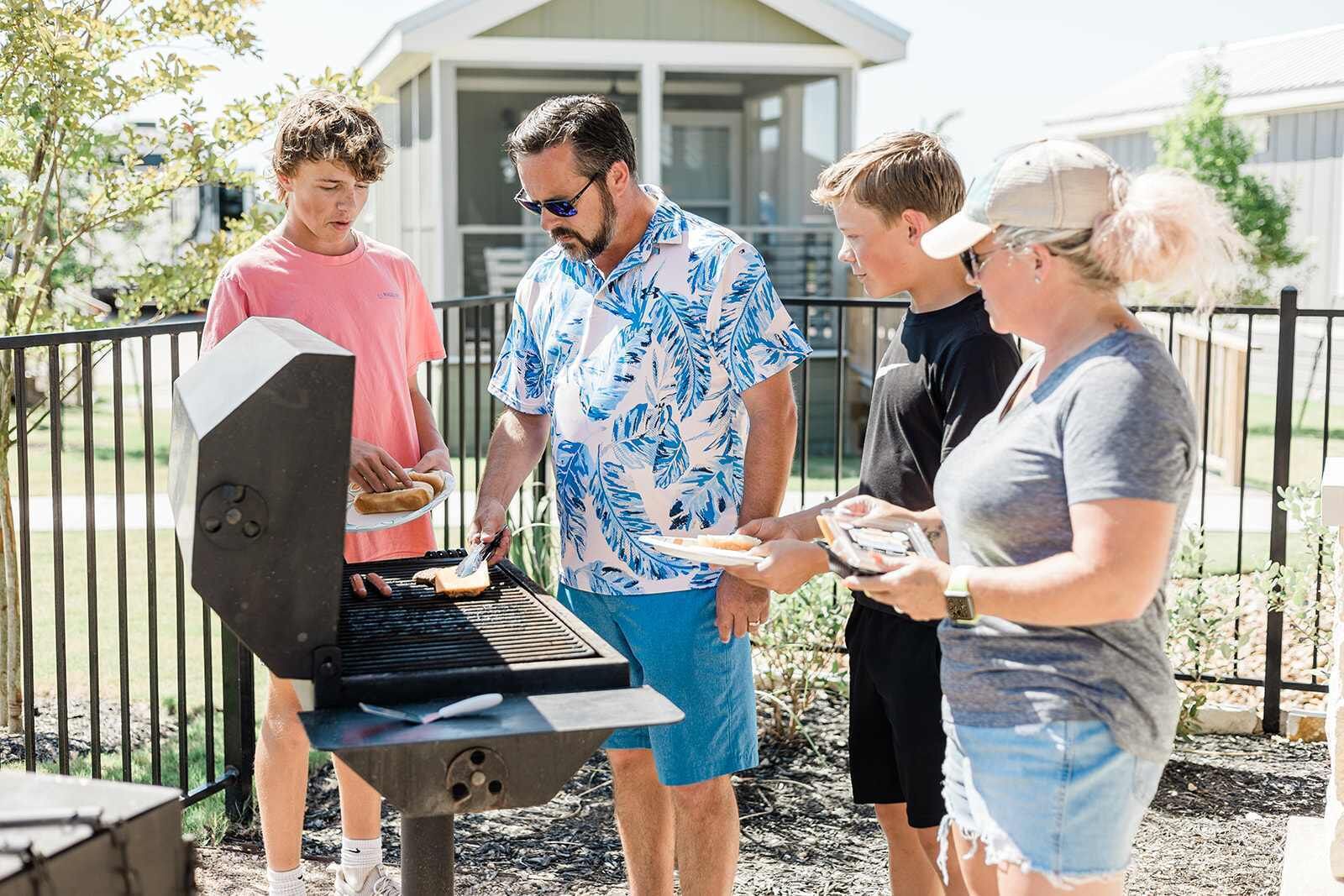 A group of people grilling outdoors with a modern house in the background.