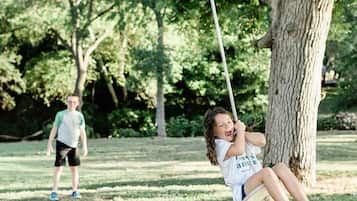 A park with a swing set, a tree, and a person walking in the background.