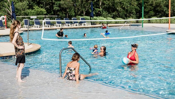 En swimmingpool med folk i vattnet, en livräddarstation och solstolar längs poolkanten.