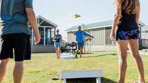 Eine Gruppe von Menschen spielt Frisbee auf einer Wiese, im Hintergrund ist ein Gebäude zu sehen.