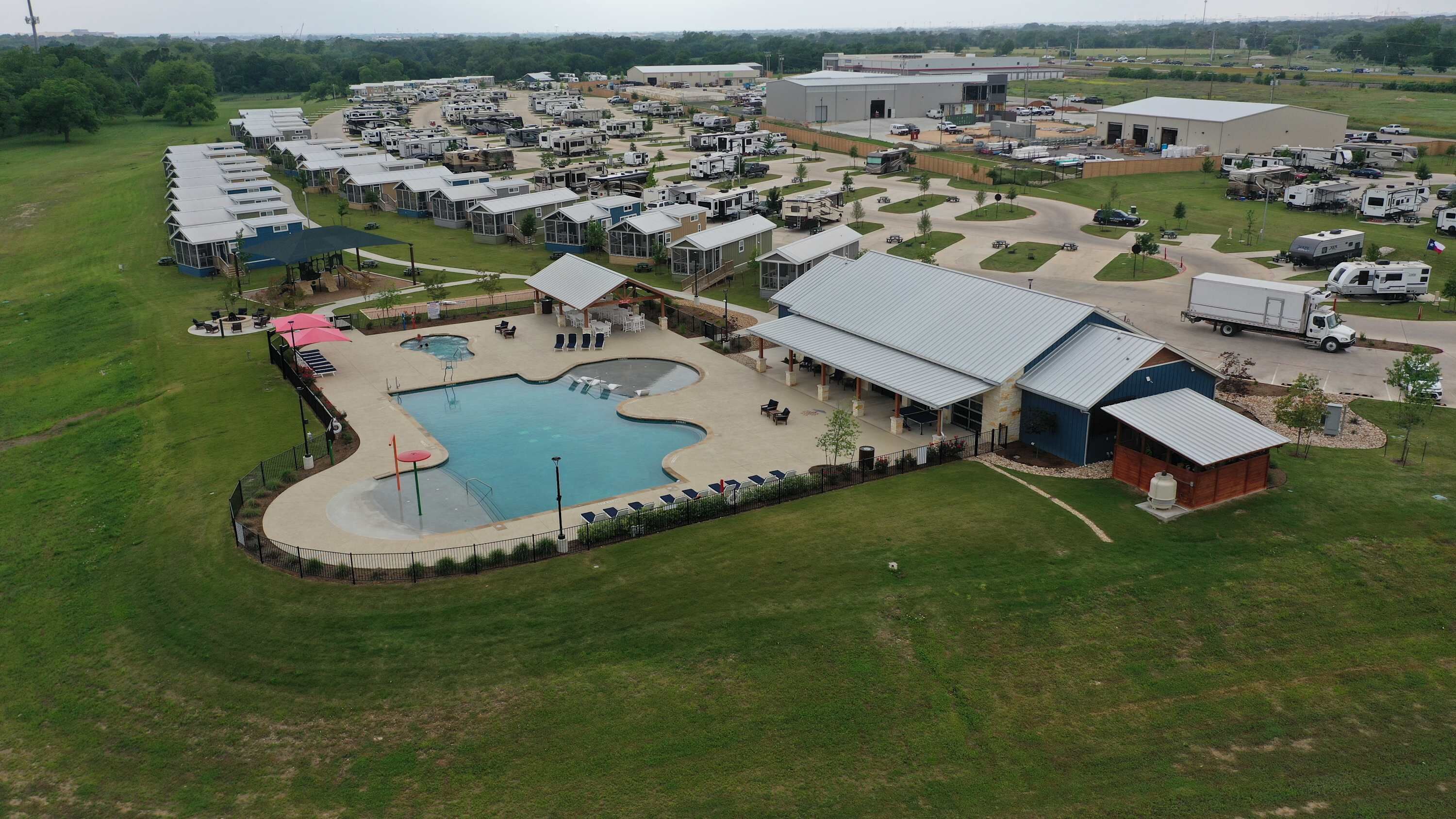 An RV park with multiple RVs, a swimming pool, and a large building.