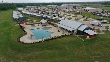 An RV park with multiple RVs, a swimming pool, and a large building.