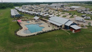 An RV park with multiple RVs, a swimming pool, and a large building.