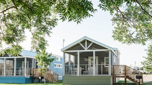 A covered outdoor area with a wooden deck, a glass enclosure, and a staircase leading to a building with a gabled roof.