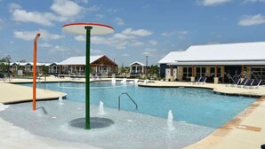 A swimming pool with water features, lounge chairs, and buildings in the background.