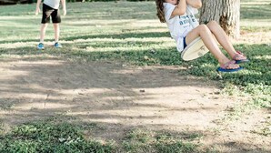 A park with a swing set, a tree, and a person walking in the background.