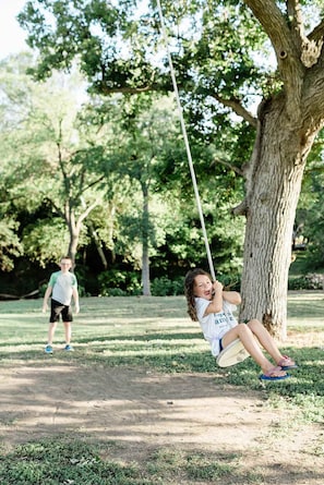 A park with a swing set, a tree, and a person walking in the background.