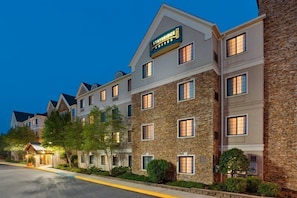 Un hotel a più piani con facciata in pietra, un cartello che indica 'Staybridge Suites' e un ingresso ben illuminato.