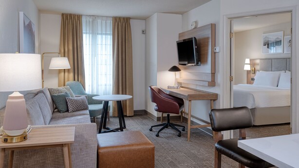 A hotel room with a bed, a desk with a chair, a sofa, a small table, and a TV on the wall.
