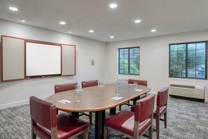 Une salle de conférence dotée d’une grande table, de chaises rouges, d’un tableau blanc et de grandes fenêtres.